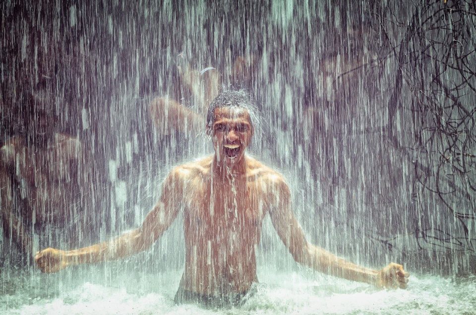 Mann betritt Wasserfall, Kaskade, Bad, Wasser tropft, starkes Wasser, Regen, wird nass